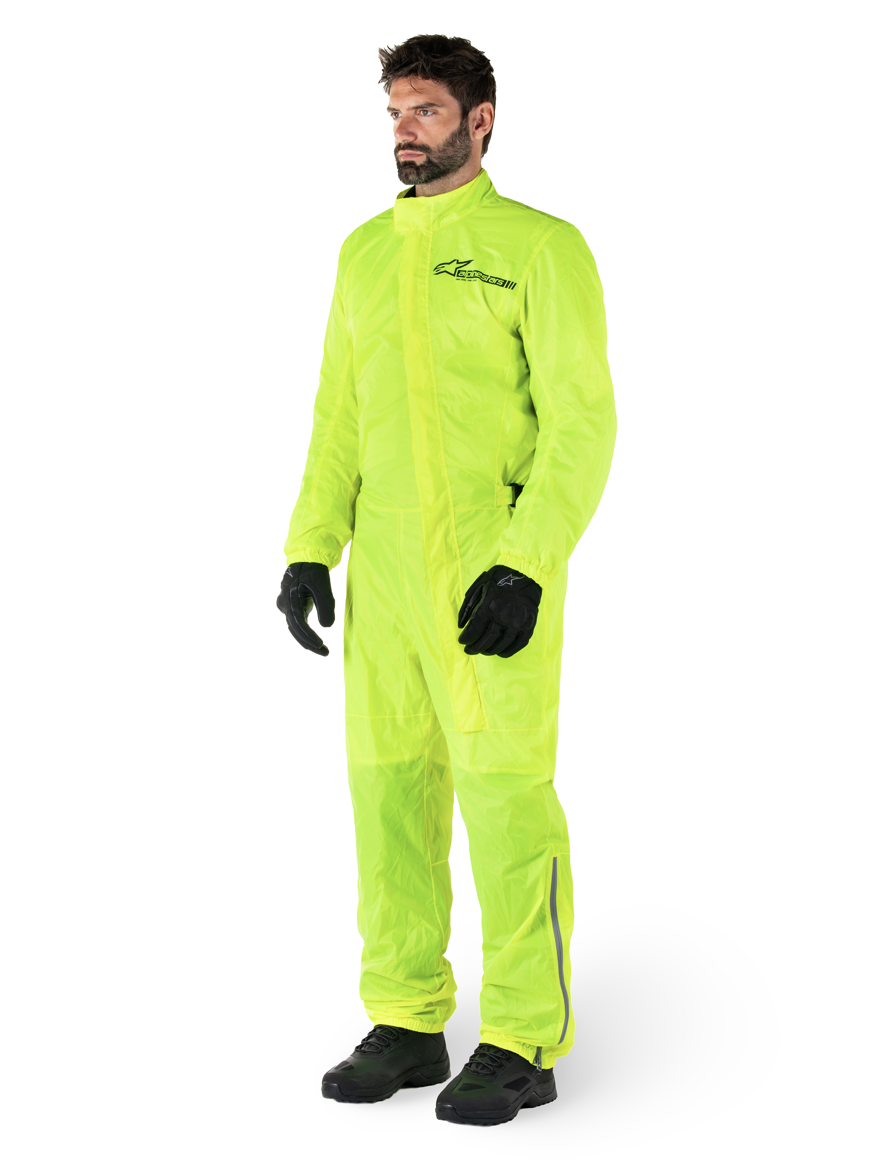 Alpinestars Hurricane Rain V2 Anzug, einteiliger wasserdichter Motorrad-Regenanzug, Gelb Fluo, getragen mit schwarzen Handschuhen und Stiefeln, mit schwarzem Alpinestars-Logo auf der Brust und reflektierenden Details an den Beinen