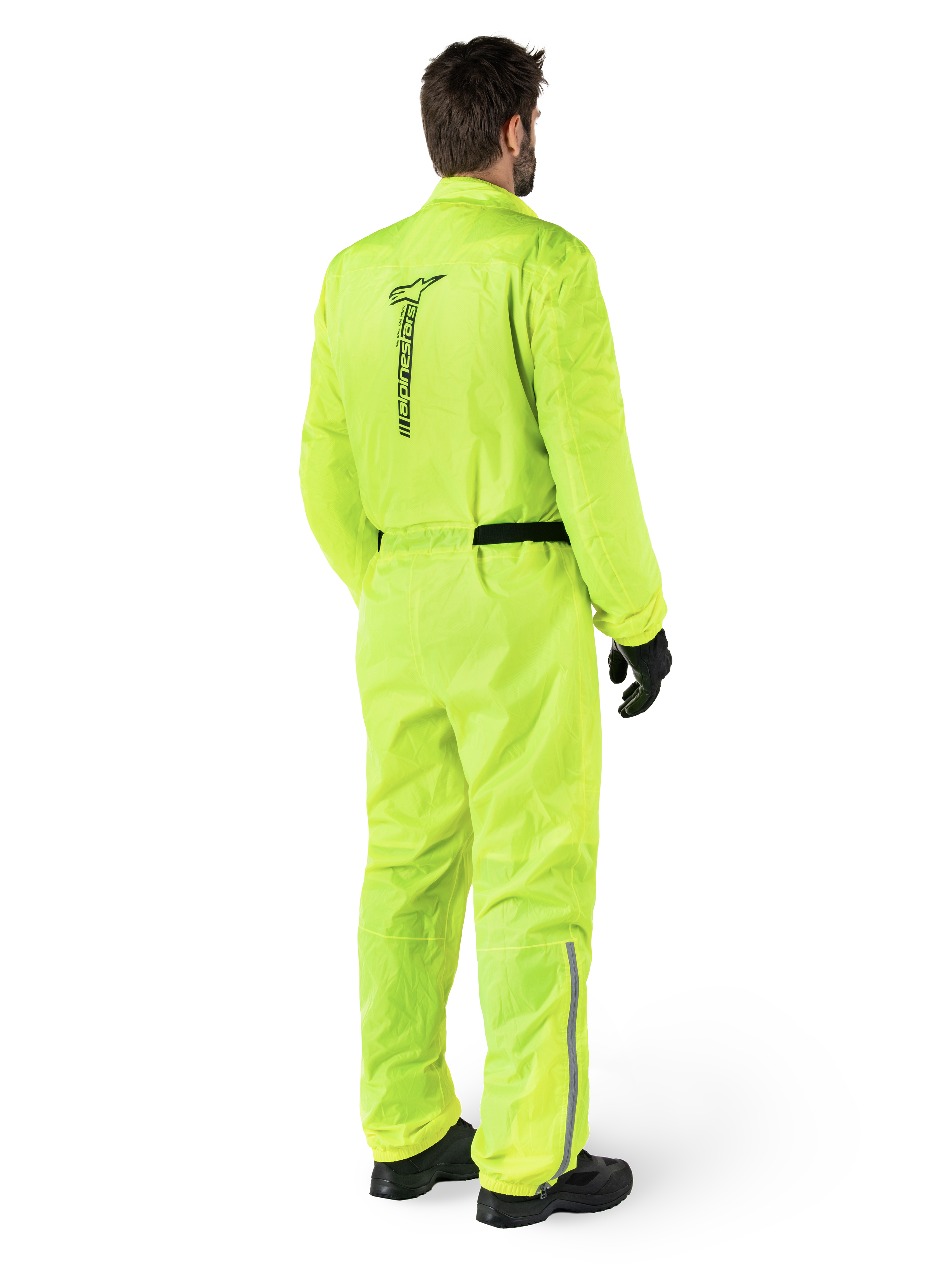 Alpinestars Hurricane Rain V2 Anzug, Gelb Fluo, Rückansicht eines Fahrers in einem einteiligen Motorrad-Regenanzug, mit schwarzem Alpinestars-Logo auf dem Rücken, schwarzem Hüftgurt und reflektierenden Streifen an den Unterschenkeln, getragen mit schwarzen Handschuhen und Stiefeln