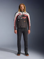 Alpinestars Axton Jacke, Motorradjacke, Schwarz, Off-White und Leuchtendes Rot, getragen von einem Model mit schwarzer Hose und Sneakern, mit einem markanten, umlaufenden Logo und einem vom Vintage-Rennsport inspirierten Design