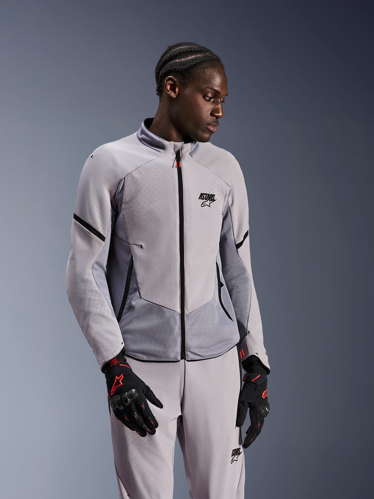 Alpinestars Aeroshell Airflow Jacke, Mittelgrau Anthrazit, getragen von einem Model mit passender Textilhose und schwarzen Handschuhen mit roten Akzenten, laserperforierte Zonen und Mesh-Einsätze für optimale Belüftung, elegantes Sport-Fit-Design für das Motorradfahren