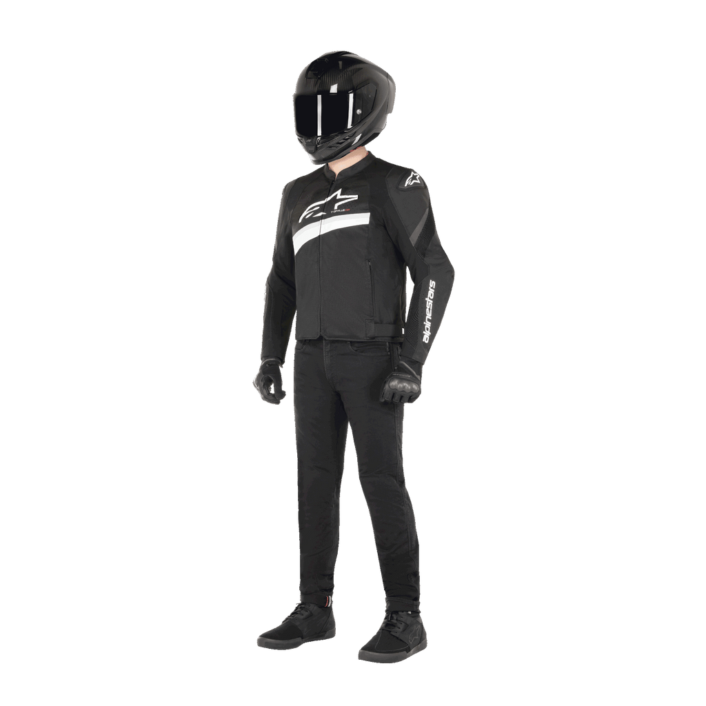 Rider wearing Alpinestars T-GP Plus R V4 Airflow Jacket in Black and White, textile motorcycle jacket with mesh panels and white Alpinestars branding, paired with a black helmet, black riding gloves, black pants, and black shoes
