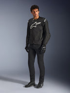 Alpinestars T-GP Air Jacket, Black textile motorcycle jacket, worn by a model with matching black pants and gloves, featuring a prominent white Alpinestars logo on the chest and shoulders, ventilated mesh panels, and a sporty race-derived fit