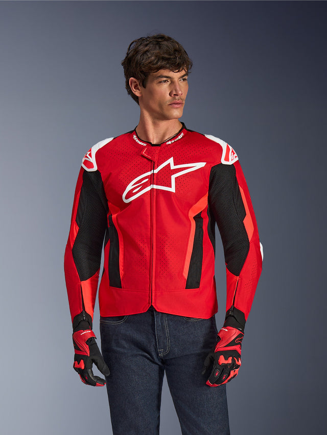 Alpinestars T-GP Air Jacke, Motorradjacke, leuchtendes Rot und Schwarz mit weißem Logo, mit perforierten Mesh-Belüftungseinsätzen, getragen mit passenden Handschuhen und dunklen Denim-Jeans, sportliches Design für Fahrten bei warmem Wetter