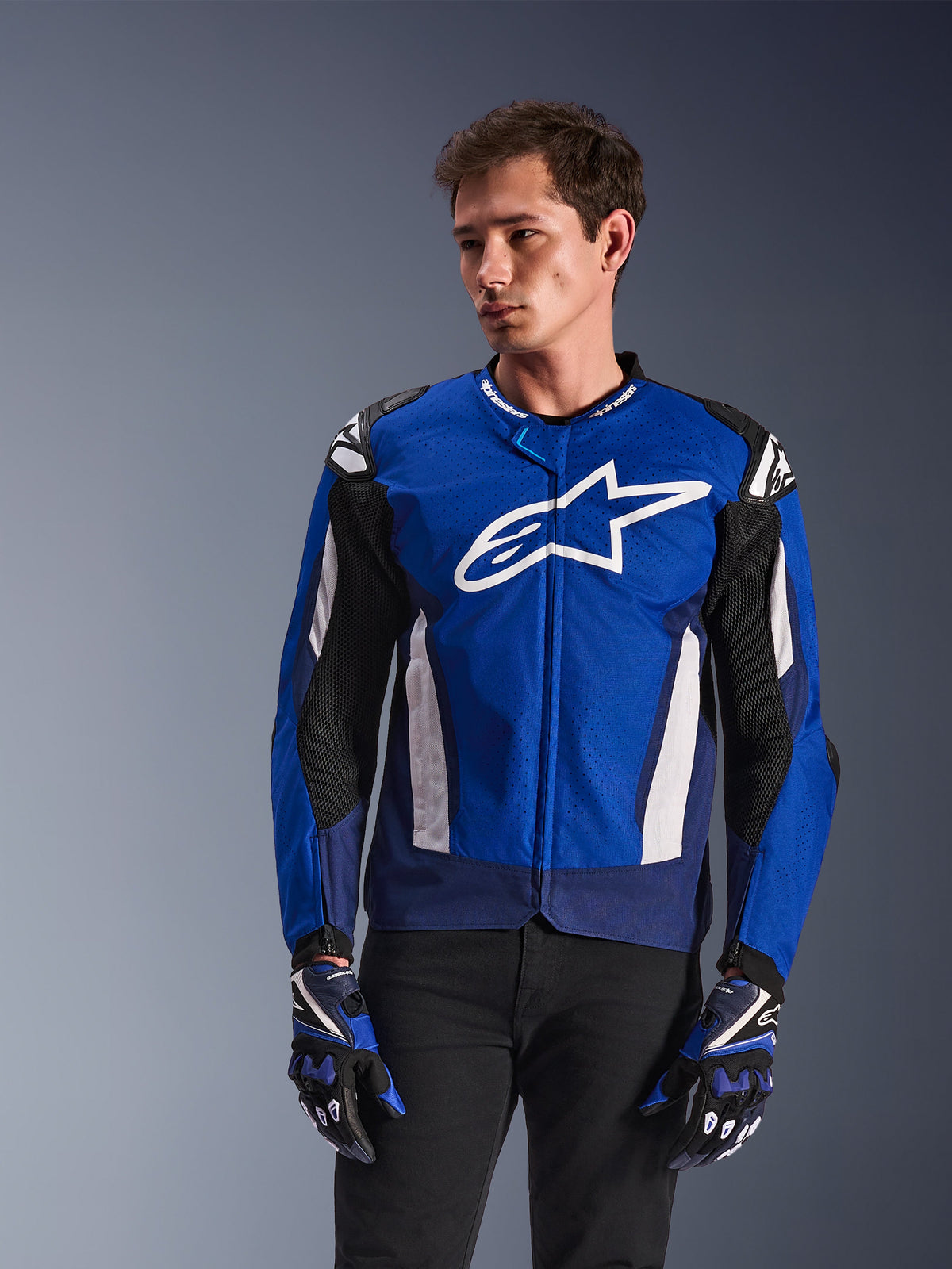 Alpinestars T-GP Air Jacke, Sport-Textilmotorradjacke, Hellblau und Navy mit weißen Akzenten, mit großem Stern-Logo auf der Brust, Mesh-Belüftungseinsätzen, getragen von einem Modell mit passenden Handschuhen und schwarzer Hose