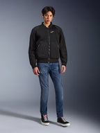Alpinestars Flight Air Jacke, Schwarz, urban inspirierte Motorradjacke im Bomber-Stil mit 3D-Mesh-Einsätzen und weißem Brustlogo, getragen von einem Model mit blauen Jeans und schwarzen Sneakern, moderne Motorradbekleidung