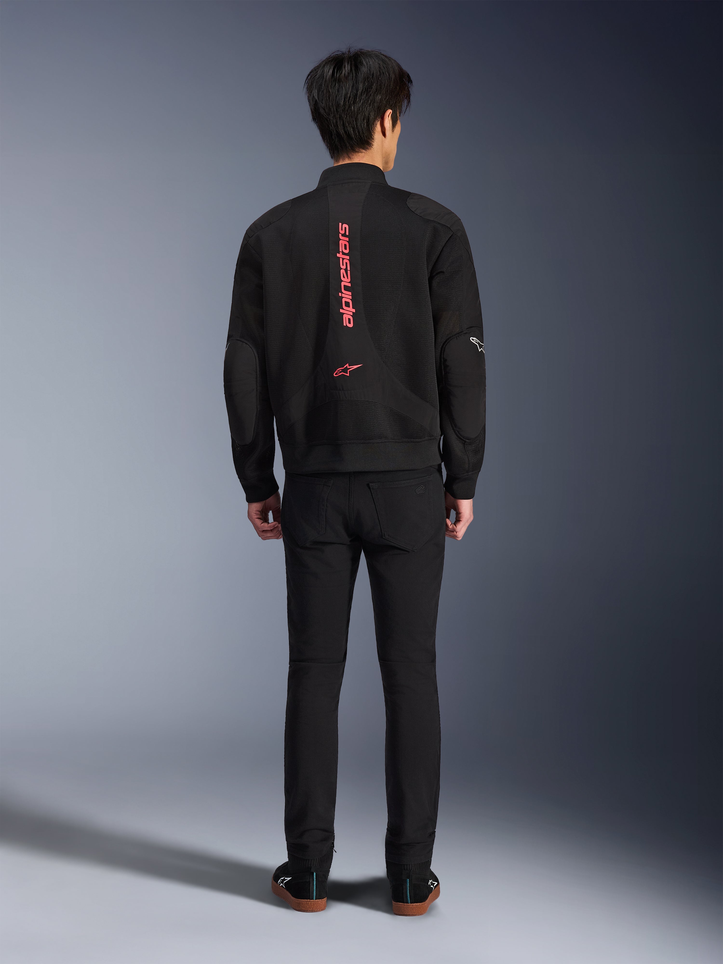 Alpinestars Flight Air Jacke in Schwarz Bright Red, Rückansicht einer urbanen Motorradjacke im Bomber-Stil, mit vertikalem rotem Alpinestars-Schriftzug und Logo auf dem Rücken, leichte 3D-Mesh-Konstruktion, kombiniert mit schwarzer Hose für einen modernen Look.