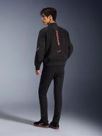 Männliches Model trägt die Alpinestars Flight Air Jacke in Black Bright Red, Rückansicht mit vertikalem rotem Branding auf dem Rücken und 3D-Mesh-Konstruktion, kombiniert mit schwarzer Hose und Sneakern, urbaner Motorrad-Stil