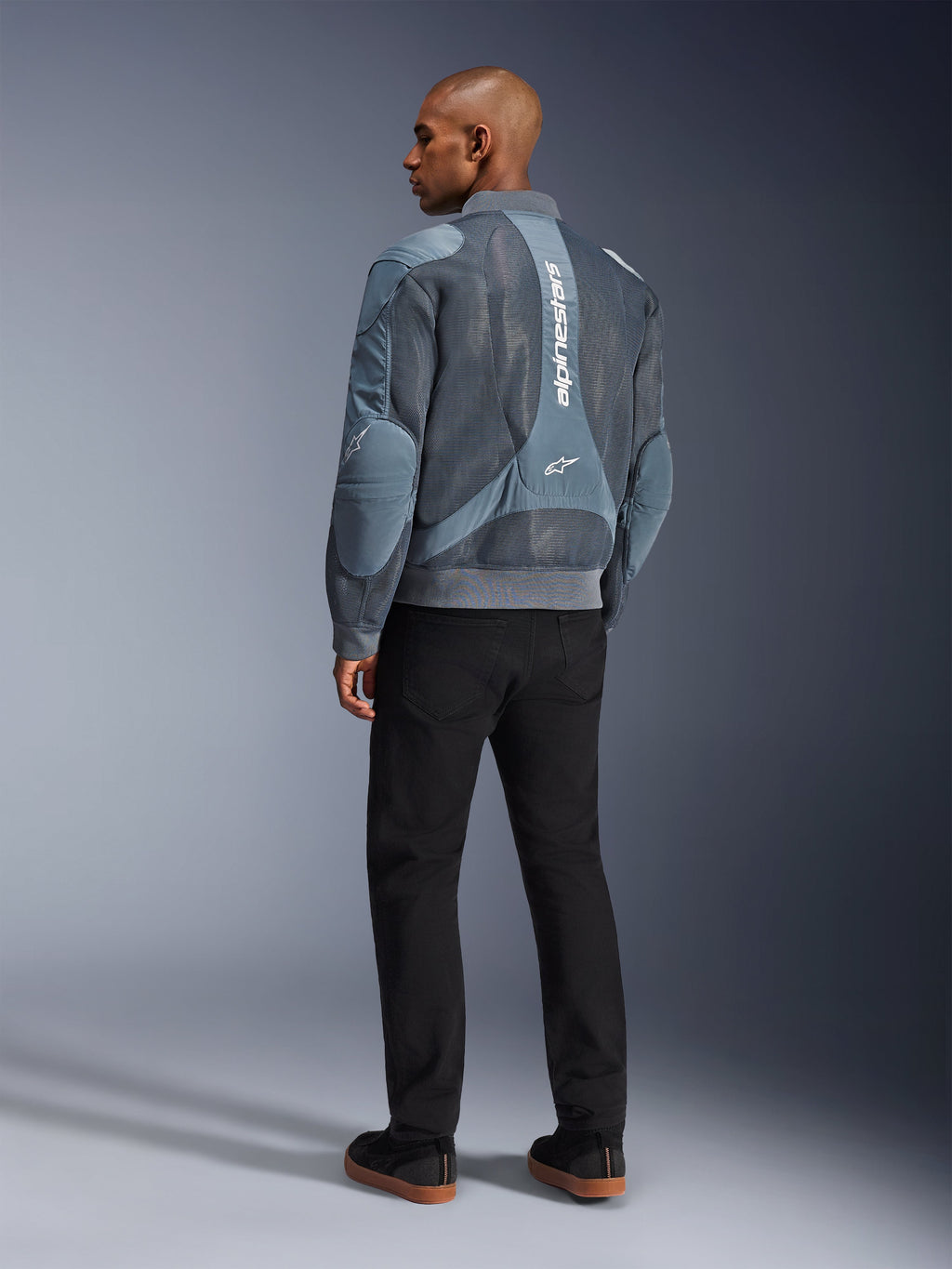 Alpinestars Flight Air Jacke, Motorradjacke in Storm Gray, Rückansicht, mit 3D-Mesh-Belüftungseinsätzen und vertikalem weißem Alpinestars-Branding, getragen mit schwarzer Hose und schwarzen Sneakern, urbaner Pendler-Stil