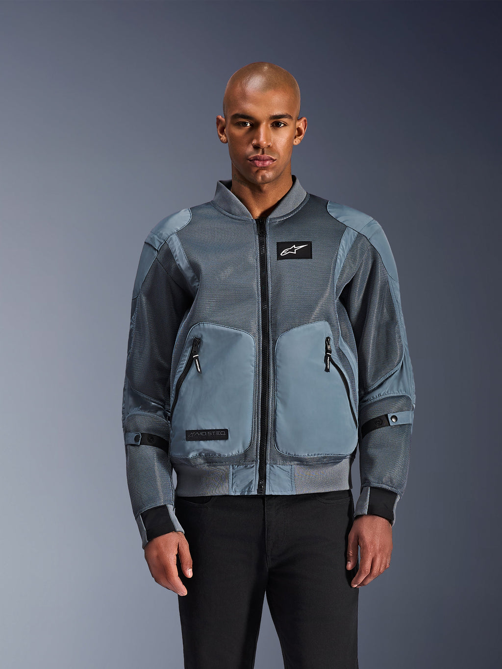Alpinestars Flight Air Jacke, urbane Bomber-Motorradjacke, Storm Gray, mit 3D-Mesh-Belüftungseinsätzen und weißem Astars Logo-Aufnäher, getragen von einem männlichen Model mit schwarzer Hose, moderne urbane Fahrbekleidung