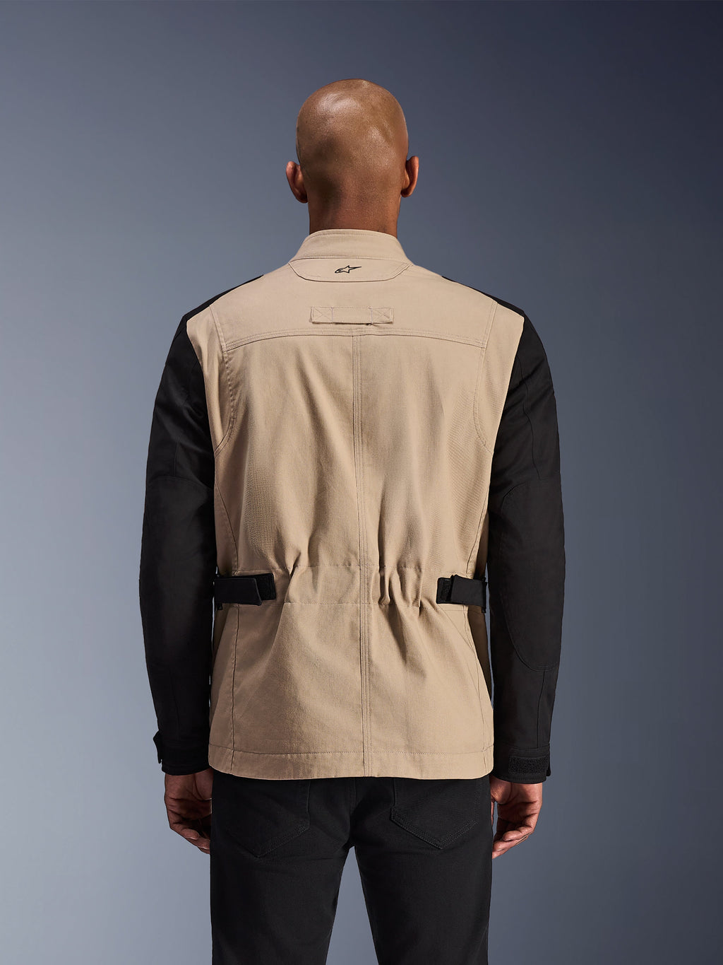 Alpinestars Dice Jacke, urbane Motorradjacke, Aluminium und Schwarz, Rückansicht an einem Modell, plissierte Schultern für Bewegungsfreiheit, verstellbare Taillenriemen, robuste Polycotton-Twill-Konstruktion.