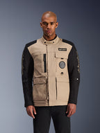 Alpinestars Dice Jacke, urbane Motorradjacke, Beige und Schwarz, robuste Workwear-Ästhetik mit mehreren Funktionstaschen und Brust-Patches, hoher Kragen mit Knopfverschluss, markantes Branding an den Ärmeln, getragen von einem männlichen Model