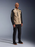 Alpinestars Dice Jacke, Urbane Motorradjacke, Aluminum Black und Tan, zweifarbiges Design mit schwarzen Ärmeln und khakifarbenem Torso, getragen von einem Model mit schwarzer Hose und schwarzen Sneakern, Workwear-inspirierte Ästhetik mit Utility-Taschen und gesticktem Branding auf dem Ärmel.