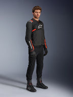 Male model wearing Alpinestars T-Sps Air V2 Jacket, Black with Red Fluo accents, paired with black motorcycle pants, black gloves, and black boots, highlighting a sporty design with mesh panels and white Alpinestars logos.