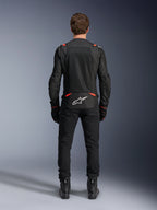 Alpinestars T-SPS Air v2 Jacket in Black and Red Fluo, rear view showing large mesh ventilation panels and white Alpinestars logo on the lower back, worn with black riding pants and boots.