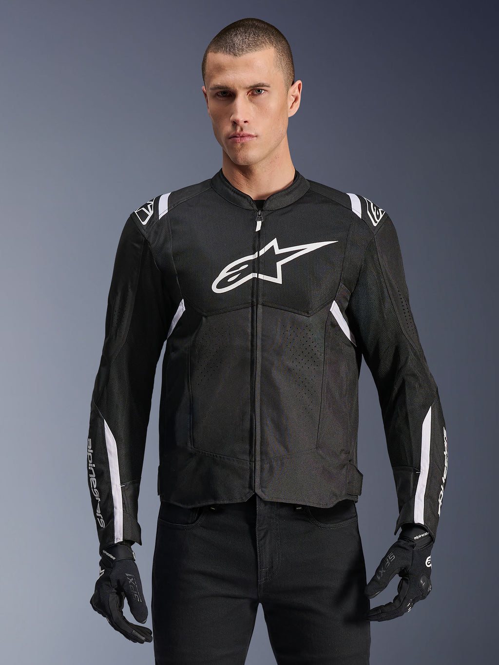 Alpinestars T-SPS Air V2 Jacke, Textil-Motorradjacke, Schwarz mit weißen Akzenten, großes weißes Brustlogo, perforiertes Mesh-Design für Belüftung, getragen mit schwarzer Hose und Handschuhen