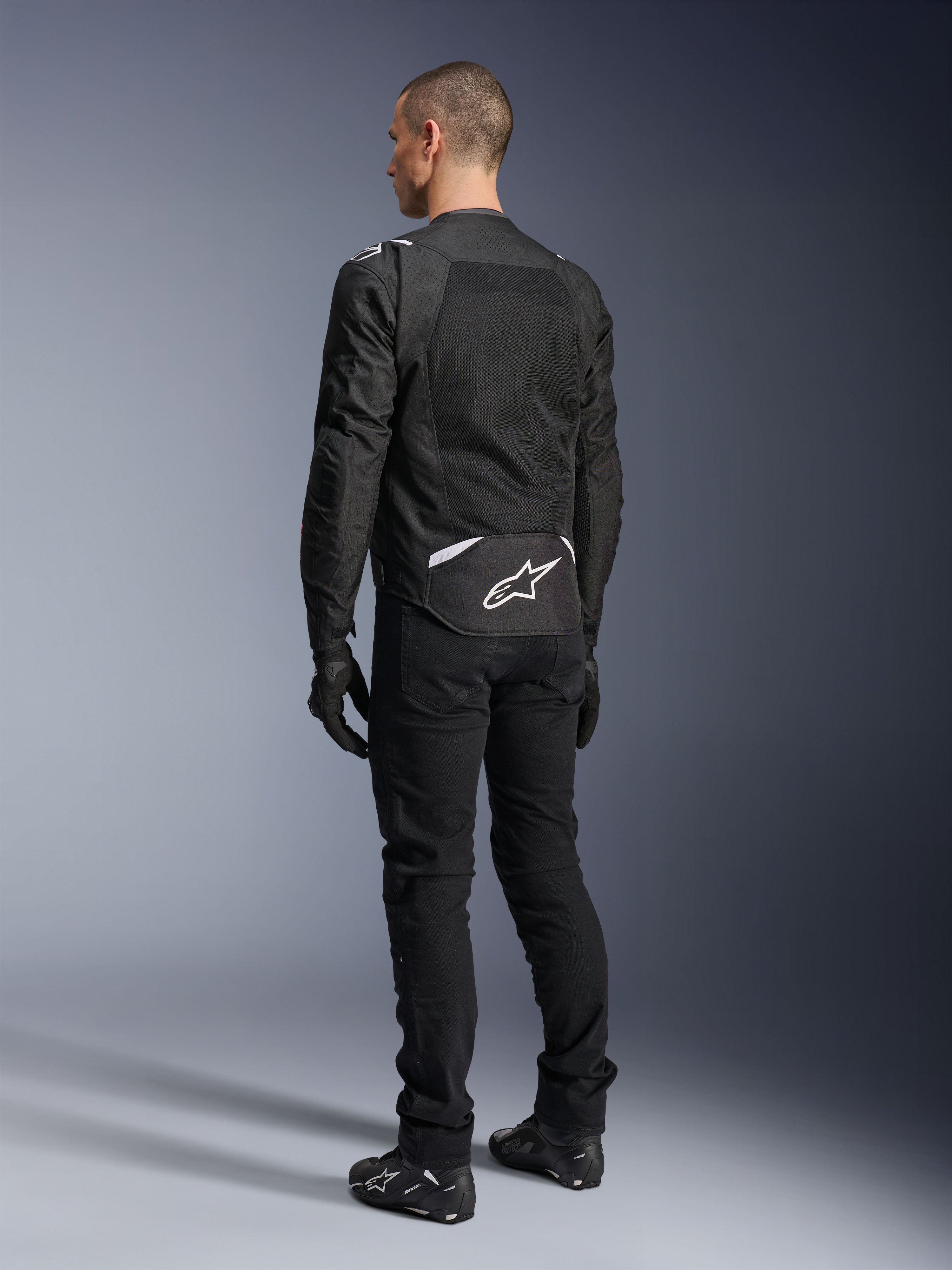Alpinestars T-Sps Air V2 Jacke, Textil-Motorradjacke, Schwarz, Rückansicht mit großem Mesh-Belüftungspanel und weißem Alpinestars-Logo am unteren Rücken, kombiniert mit schwarzer Motorradhose und Handschuhen für einen sportlichen urbanen Look.