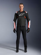 Male model wearing Alpinestars T-Sps Air V2 Jacket in Black White Red Fluo, featuring large tech mesh panels and bold white branding on the chest and sleeves, paired with black technical riding pants and gloves, urban sport motorcycle gear