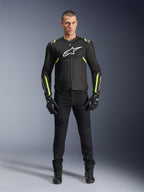Alpinestars T-Sps Air V2 Jacke, Schwarz und Gelb Fluo, Textil-Motorradjacke mit Mesh-Einsätzen, getragen von einem männlichen Model mit schwarzer Hose und Handschuhen, weißes Alpinestars-Logo auf der Brust, urbane Sport-Motorradausrüstung