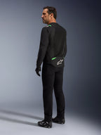 A man wearing the Alpinestars T-SPS Air V2 Jacket in Black Fluo Green, shown from a back and side profile view, styled with black riding pants and motorcycle shoes. The jacket features ventilated tech mesh panels, bright green accents on the shoulders and lower back, and a white star logo on the rear tail.