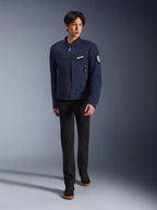 Männliches Model in Alpinestars Bruiser Jacke in Dark Blue, urbane Textil-Motorradjacke, kombiniert mit schwarzer Hose und schwarzen Sneakern, Workwear-inspirierte Ästhetik mit Reißverschlusstaschen und rundem Ärmel-Patch, zeitgemäße Streetwear für das Motorradfahren.