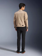 Rückansicht eines Modells, das die Alpinestars Bruiser Jacke in Braun trägt, eine urbane Motorradjacke mit von Workwear inspiriertem Design, mit Metallösen am Rücken und Taillenverstellern, kombiniert mit schwarzer Hose und Sneakern, moderner Street-Riding-Stil.