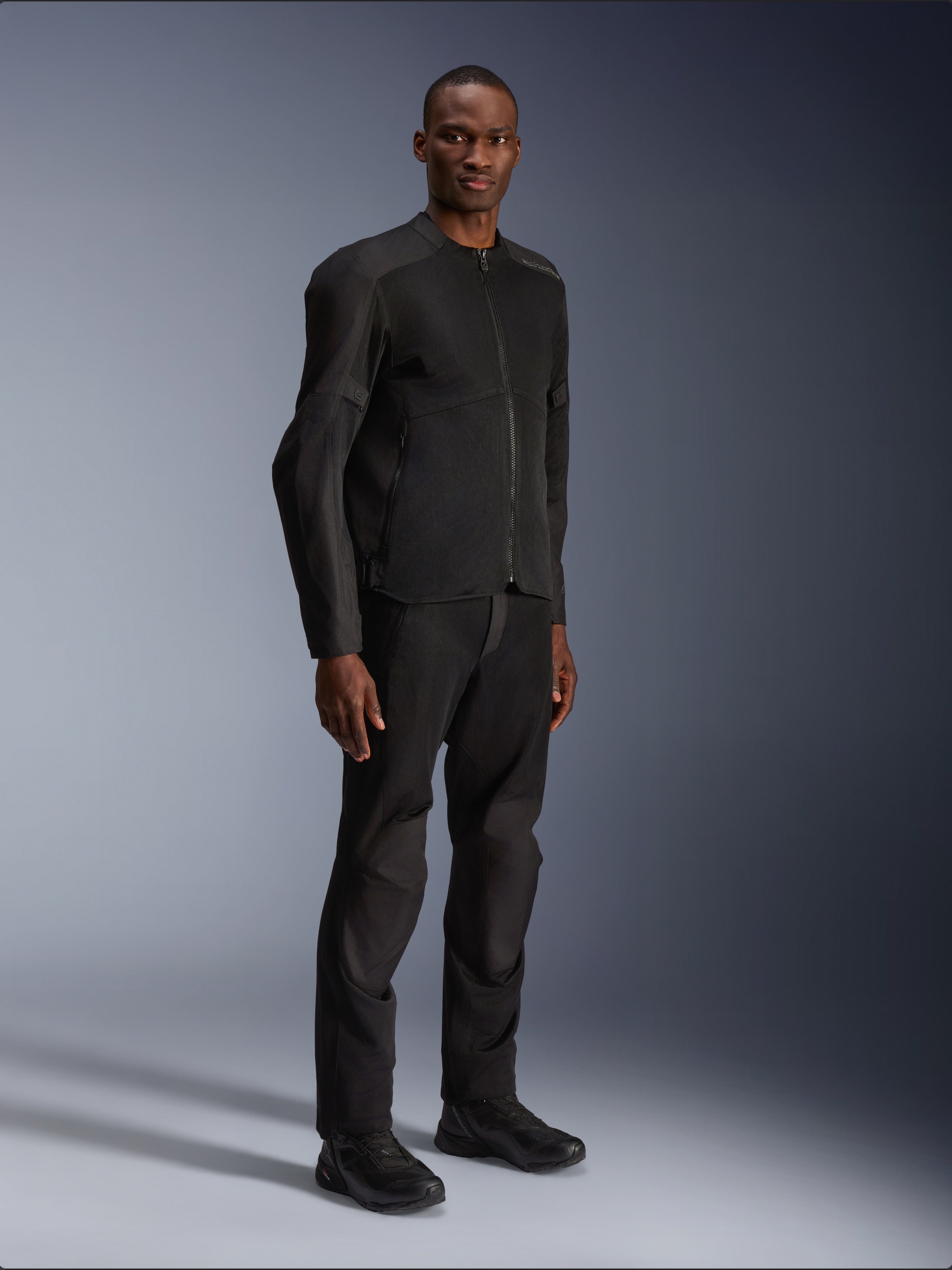Alpinestars C-1 Air Jacke, Schwarz, getragen von einem Model mit passender schwarzer Motorradhose und Schuhen, mit großen Tech-Mesh-Einsätzen für Luftzirkulation, cleanes urbanes Design mit schmaler Passform.