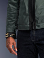 Alpinestars Ignite Air Jacke in Urban Grau, Nahaufnahme des Mesh-Gewebe-Ärmels und des schwarzen Ärmelbunds mit goldenen Streifen und Stern-Logo, getragen mit dunkelblauer Denim-Jeans, moderne urbane Motorradbekleidung.