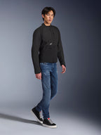 Alpinestars Provoke Jacke, Urbane Motorradjacke, Schwarz, getragen von einem männlichen Model mit blauen Jeans und schwarzen Sneakern, technisches Textildesign mit kleinem Alpinestars-Logo, Ganzkörper-Lifestyle-Aufnahme für zeitgenössisches Fahren in der Stadt
