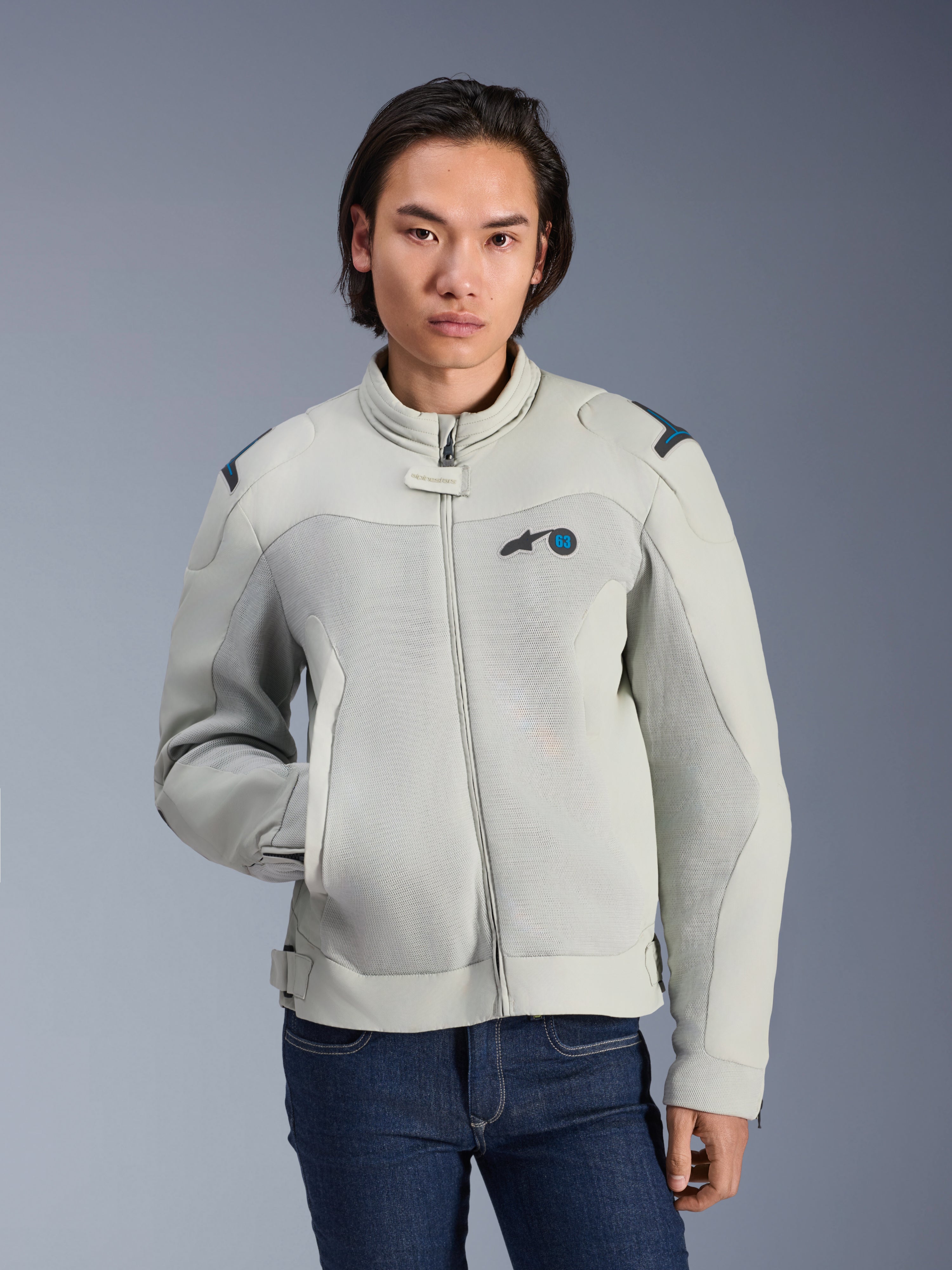 Alpinestars Circal-1 Air Jacke, Metallgrau und Methylblau, urbane Motorradjacke mit Mesh-Belüftungseinsätzen, Frontreißverschluss und gepolstertem Kragen, getragen von einem Model mit blauen Jeans, futuristisches nachhaltiges Design für Sommerfahrten