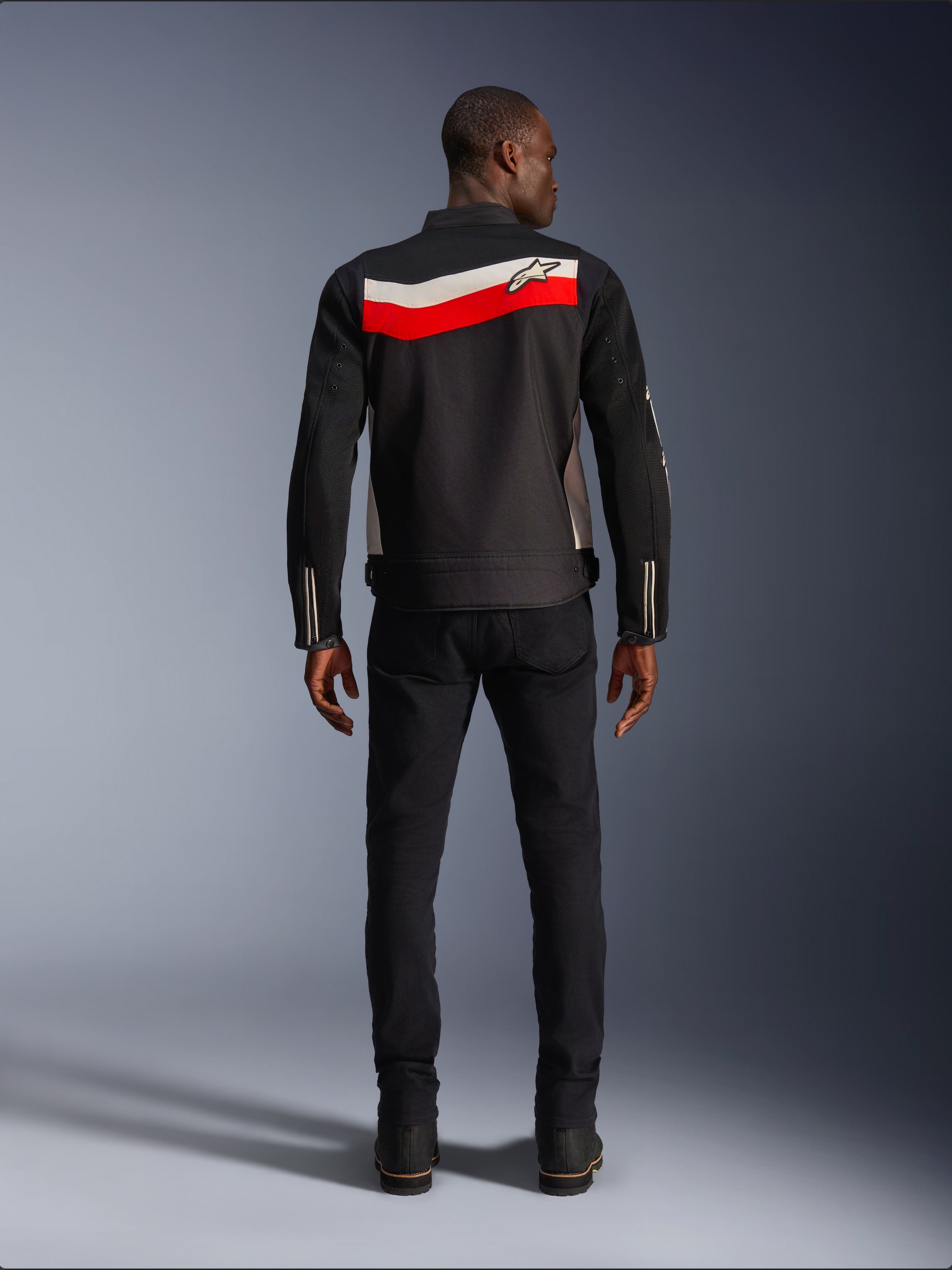 Alpinestars T-Dyno Air Jacke, Motorrad-Textiljacke für Herren, Rückansicht, Schwarz mit leuchtend roten und ecrufarbenen horizontalen Streifen auf dem Rücken, Alpinestars-Logo auf der Passe, getragen mit schwarzer Hose und Stiefeln, atmungsaktive 3D-Mesh-Konstruktion