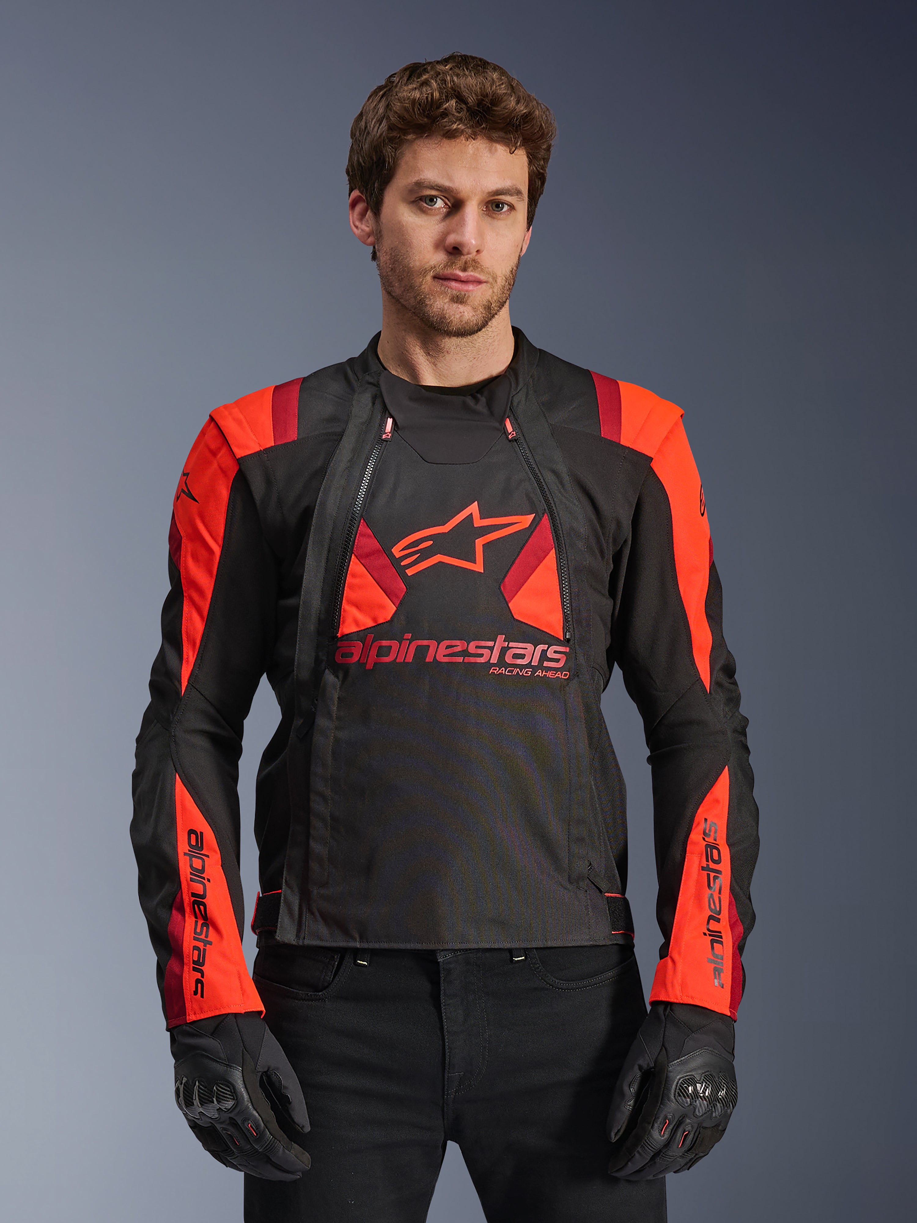 Alpinestars T-Stunt Air Jacke, Textil-Motorradjacke, Schwarz, Red Fluo und Dunkelrot, mit großem Stern-Logo und Mesh-Einsätzen für Luftzirkulation, getragen von einem Model mit schwarzen Handschuhen