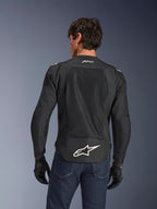 Alpinestars FQ20 T-SPS Air V2 Monster Jacke, Schwarz, Rückansicht mit großen Mesh-Belüftungseinsätzen und weißem Alpinestars-Logo am unteren Rücken, getragen mit blauen Jeans und schwarzen Motorradhandschuhen, urbaner Sport-Fahrstil.