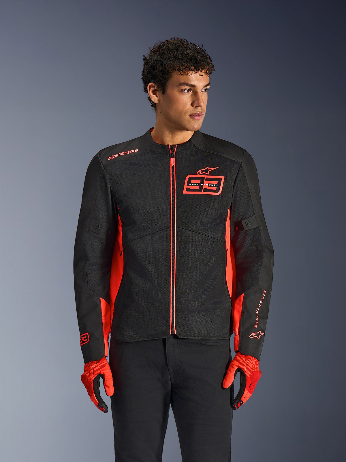 Alpinestars MM93 C-1 Air Jacke, urbane Motorradjacke, Red Fluo und Schwarz, getragen von einem Model mit passenden roten Handschuhen und schwarzer Hose, mit markantem 93 Marc Marquez Brust-Logo und Mesh-Einsätzen für Belüftung