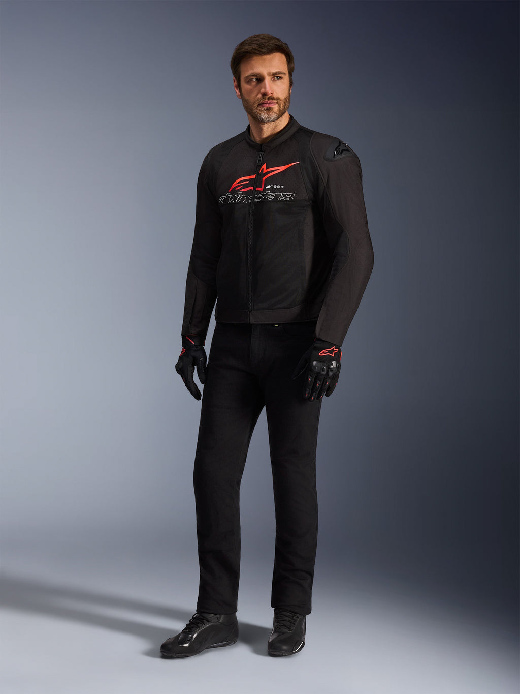 Male model wearing the Alpinestars SMX Air Jacket in Black Bright Red White, styled with black technical pants, black and red gloves, and black riding shoes, featuring a prominent red chest logo and white branding, full-body studio shot for sport motorcycling gear