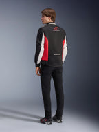 Alpinestars Monza Sport Jacket, textile motorcycle jacket, Black Bright Red and White, back view of model featuring red side panels and white sleeve accents, Alpinestars logo and 'ONE GOAL. ONE VISION.' text, paired with black pants and riding shoes for a sport-inspired look