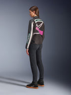 Alpinestars Idles Damenjacke, Motorradjacke, Schwarz, Off-White und Lila, Rückansicht am Modell, mit großem umlaufendem Alpinestars-Logo und von Vintage-Rennsport inspiriertem Design, kombiniert mit dunklen Jeans und schwarzen Schuhen.