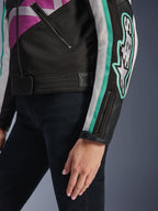 Alpinestars Idles Damenjacke, Nahaufnahme von Ärmel und seitlichem Torso, Schwarz mit lila, weißen und türkisfarbenen Akzenten, mit auffälligem Alpinestars-Logo am Arm, Ärmelbündchen mit Reißverschluss und Druckknopf sowie Taillenverstellriemen, vintage-inspirierte Motorradbekleidung.
