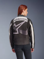 Alpinestars Idles Damenjacke, Schwarz und Off-White, Rückansicht mit großem grauen Stern-Logo und Alpinestars-Schriftzug, getragen von einem rothaarigen Model, vintage-inspirierte urbane Motorradjacke mit Akkordeon-Einsätzen.