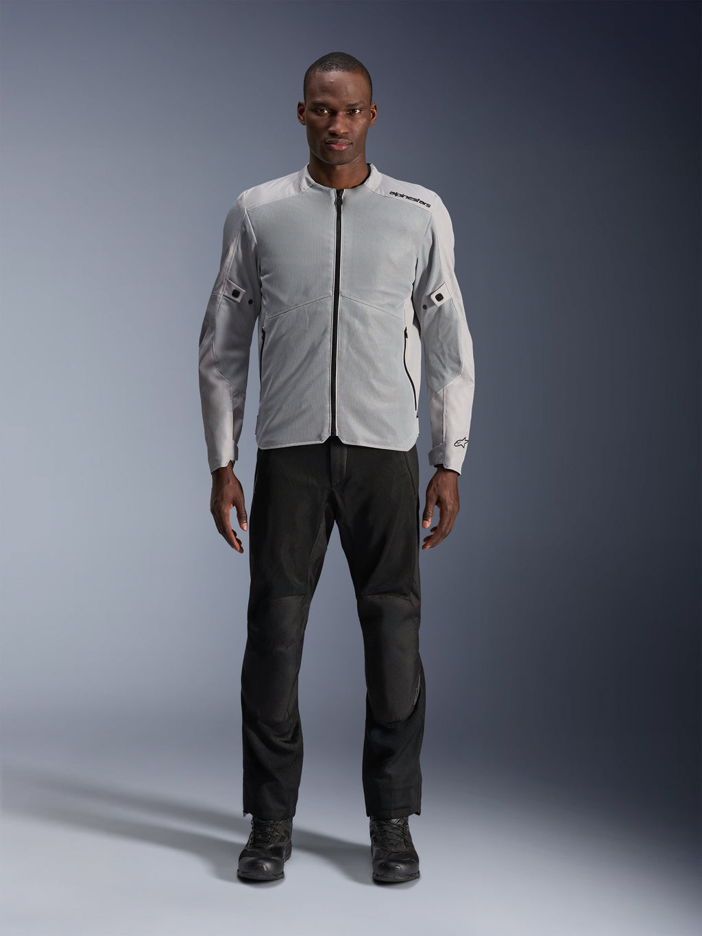 Alpinestars C-1 Air Jacke in Silber, urbane Textil-Motorradjacke für Herren mit belüfteten Mesh-Einsätzen, getragen von einem Model mit schwarzer Motorradhose und schwarzen Stiefeln, moderner Pendler-Stil