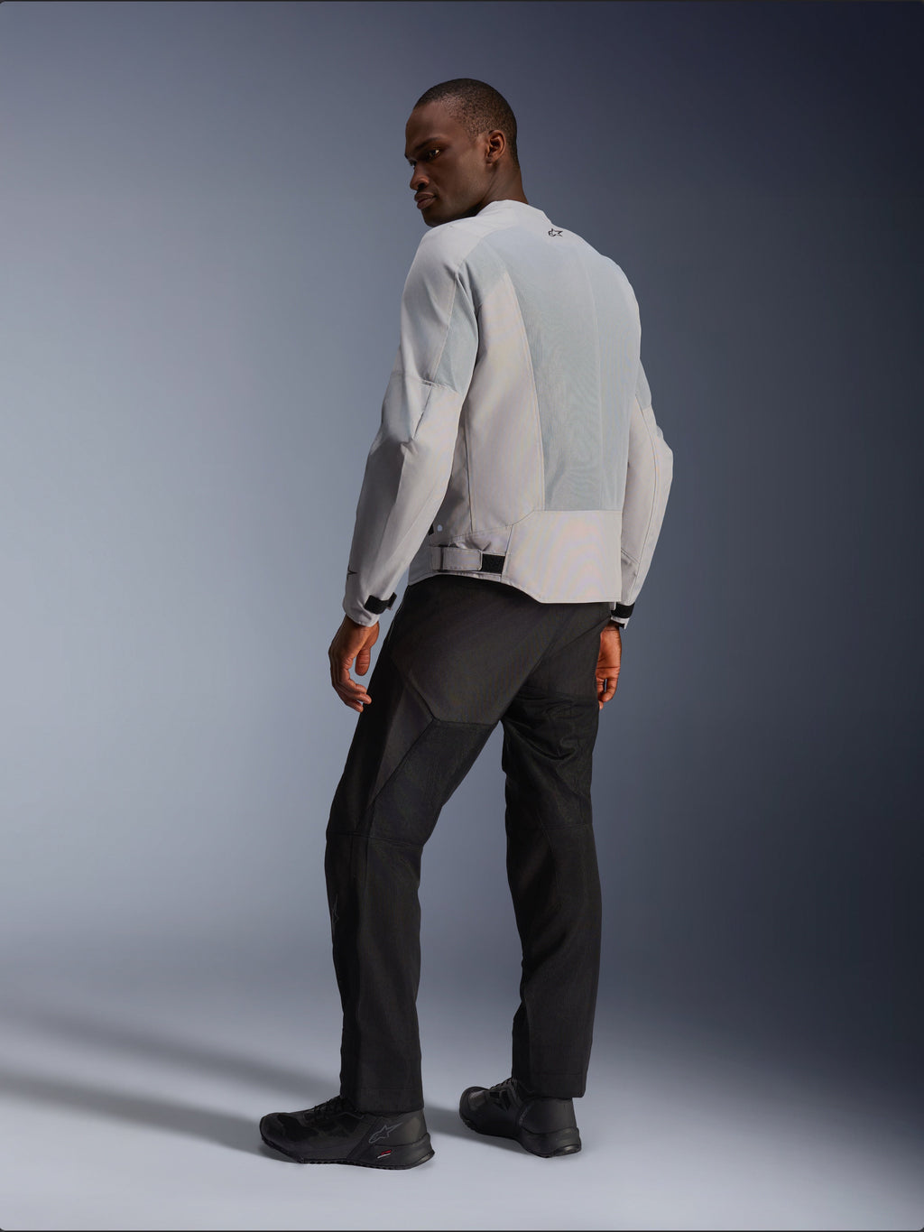 Alpinestars C-1 Air Jacke, Silber und Grau, Rückansicht an einem Modell, mit belüfteten Tech-Mesh-Einsätzen und reflektierenden Logos, getragen mit schwarzer Hose und Schuhen, urbane zeitgemäße Motorradausrüstung