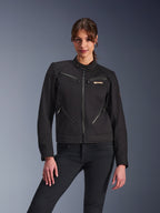 Alpinestars Stella Grace Damenjacke, Urbane Motorradjacke, Schwarz, Vorderansicht, mit mehreren Reißverschlusstaschen und einem Druckknopfkragen, kombiniert mit schwarzen Jeans, moderne Lifestyle-inspirierte Schutzausrüstung für Damen