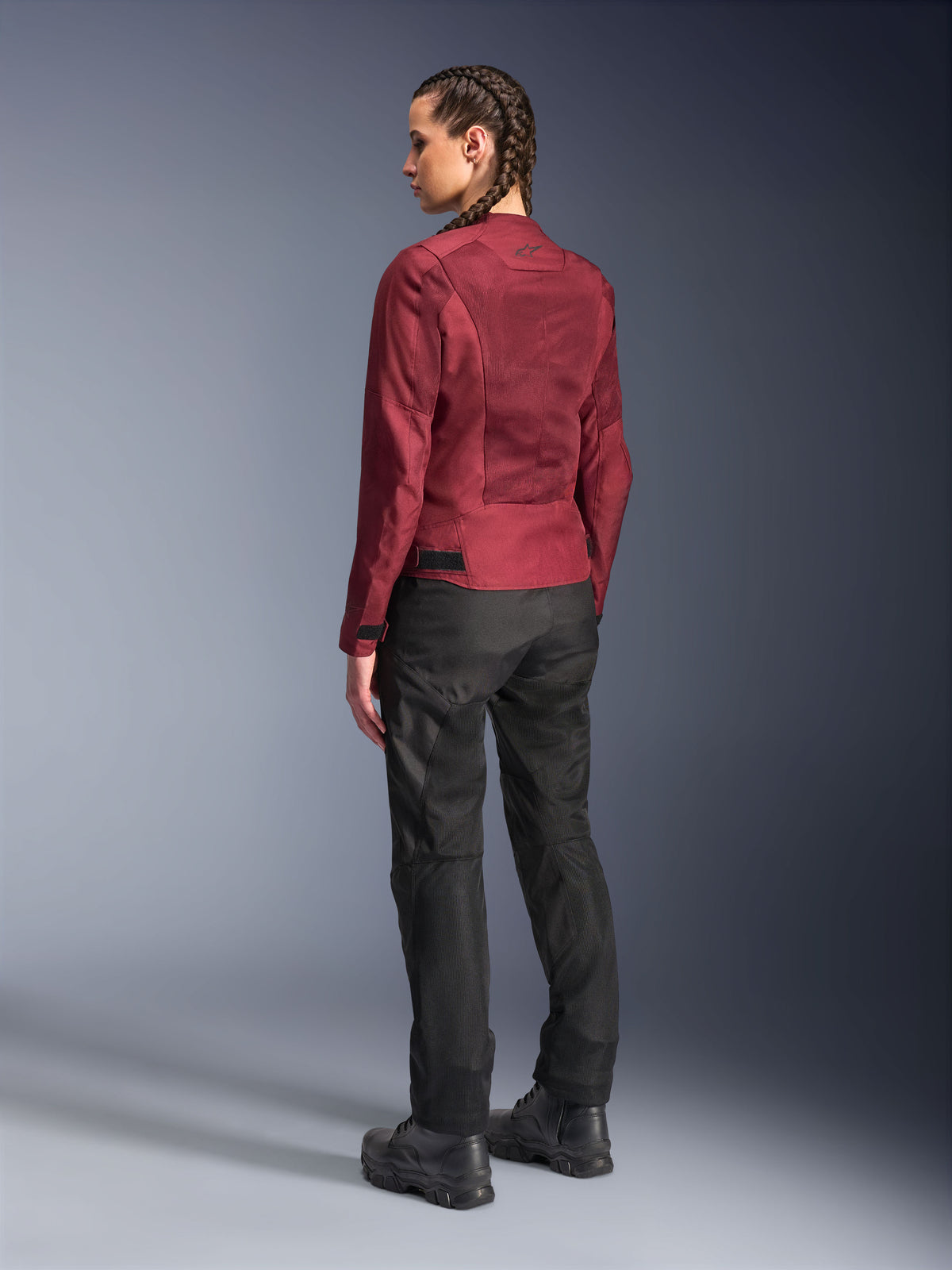 Motorradfahrerin in Alpinestars Stella C-1 Air Jacke in Burgund und Stella C-1 Air Hose in Schwarz, Ganzkörper-Rückansicht, urbane Motorradausrüstung mit technischen Mesh-Einsätzen, kombiniert mit schwarzen Motorradstiefeln