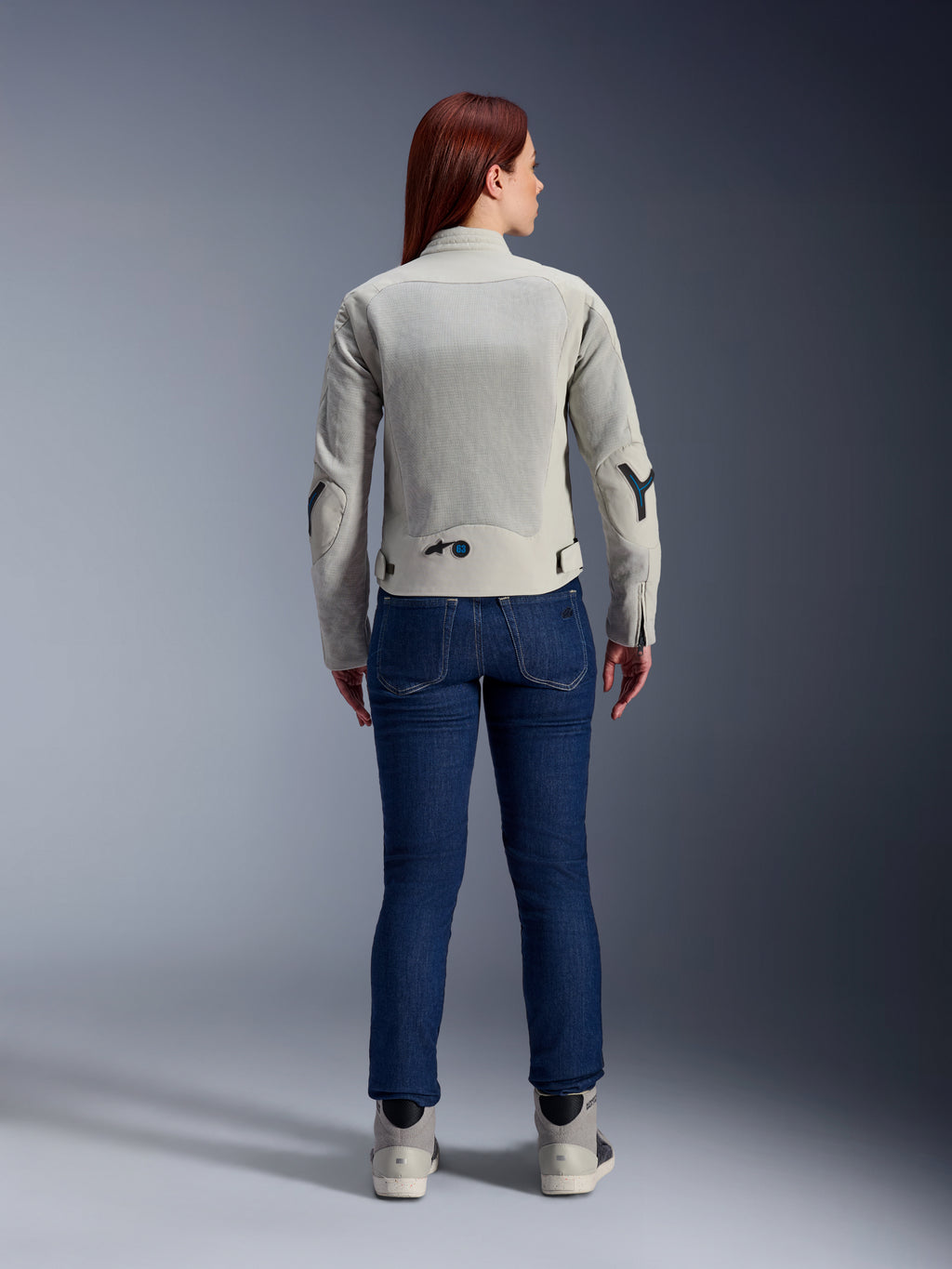 Alpinestars Stella Circal-1 Air Damenjacke in Metal Gray und Methyl Blue, Rückansicht, mit großen Mesh-Belüftungseinsätzen an Rücken und Armen, kombiniert mit dunkelblauen Jeans und grauen Motorradschuhen für einen modernen urbanen Motorrad-Look.