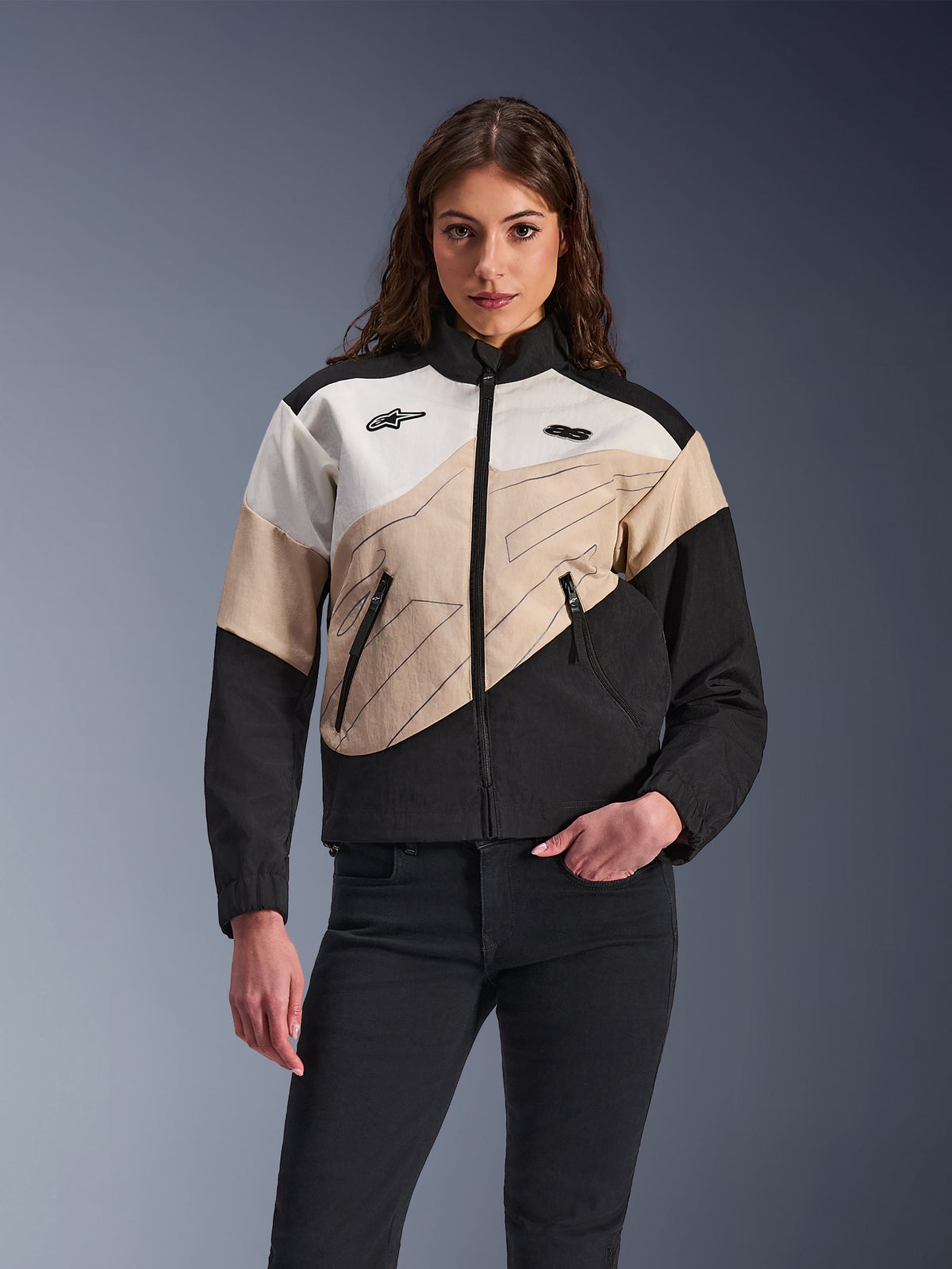 Alpinestars Stella Moshell Jacke, urbane Motorradjacke für Damen, asymmetrisches Color-Block-Design in Schwarz, Sand und Off-White, mit Frontreißverschluss und Reißverschlusstaschen, präsentiert mit einer schwarzen Hose für einen modernen Streetwear-Look.