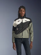 Frau trägt die Alpinestars Stella Moshell Jacke, urbane Motorradjacke in Black Fur, Grau, Off-White und Pink, asymmetrisches Design mit technischen Grafiken, pinkfarbene Zipper-Pulls und Alpinestars-Logos, zeitgenössischer Streetwear-Stil für urbane Fahrerinnen.
