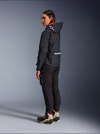 Alpinestars Actea Women's Pants, Black, modern motorcycle pants with a tapered fit and thigh cargo pocket, shown from a side-rear perspective on a model wearing a dark hooded jacket and riding boots, urban riding style.