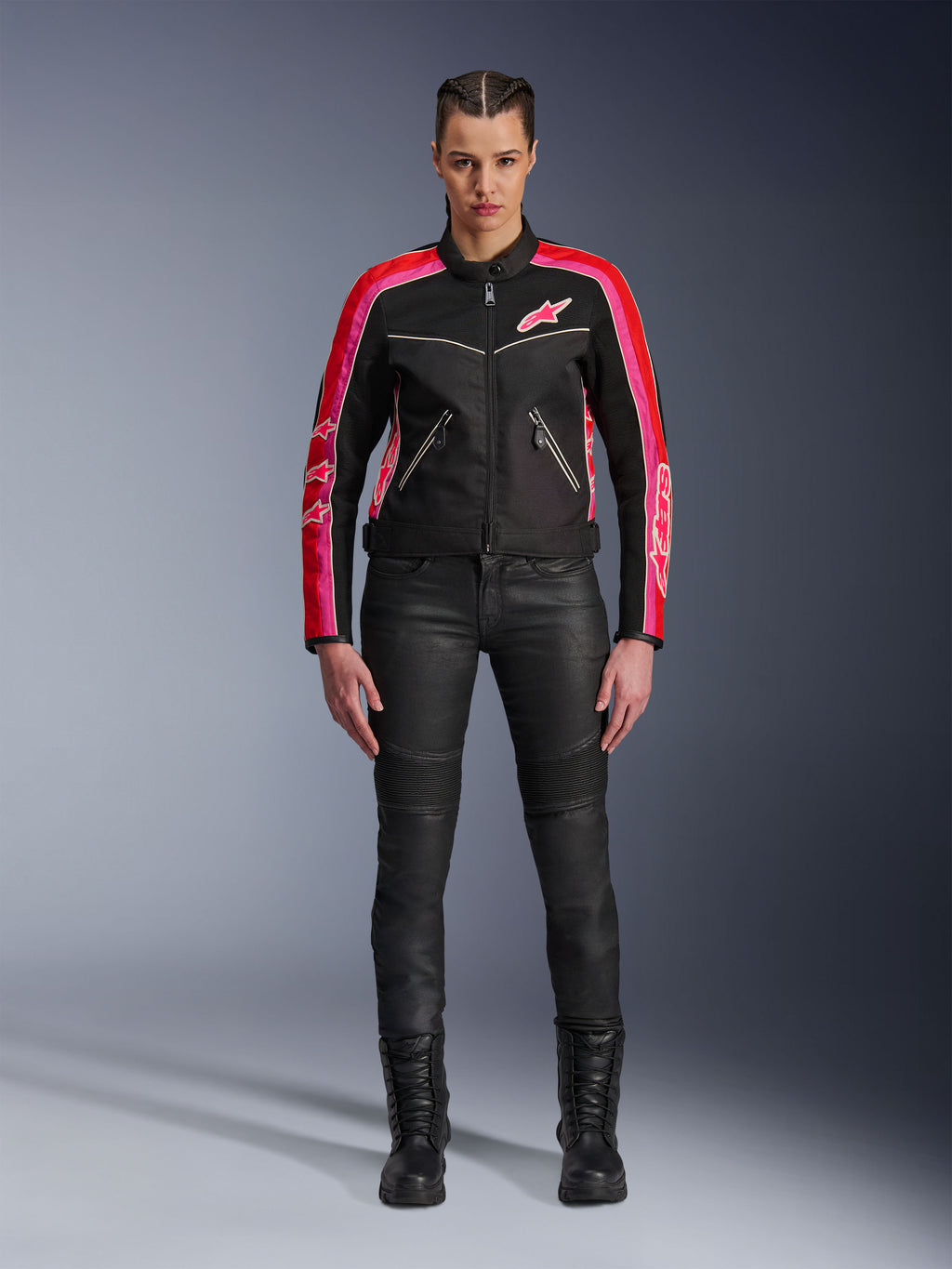 Motorradfahrerin in der Alpinestars Stella T-Dyno Air Jacke, Schwarz mit hellroten und fuchsiafarbenen Akzenten, kombiniert mit schwarzer Motorradhose und Schnürstiefeln, mit 3D-Mesh-Einsätzen, taillierter Passform und pinkfarbenen Stern-Logos, urbanes Motorrad-Outfit