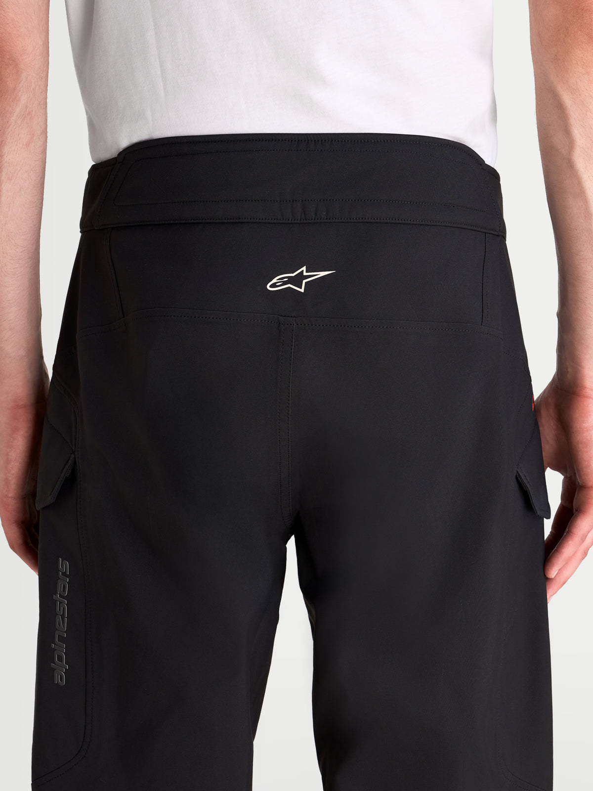 Alpinestars Juggernaut V 2 Drystar Hose, urbane wasserdichte Herren-Motorradhose in Schwarz, Rückansicht mit hochgeschnittenem Bund, weißem Astar-Logo und Cargotaschen an Model