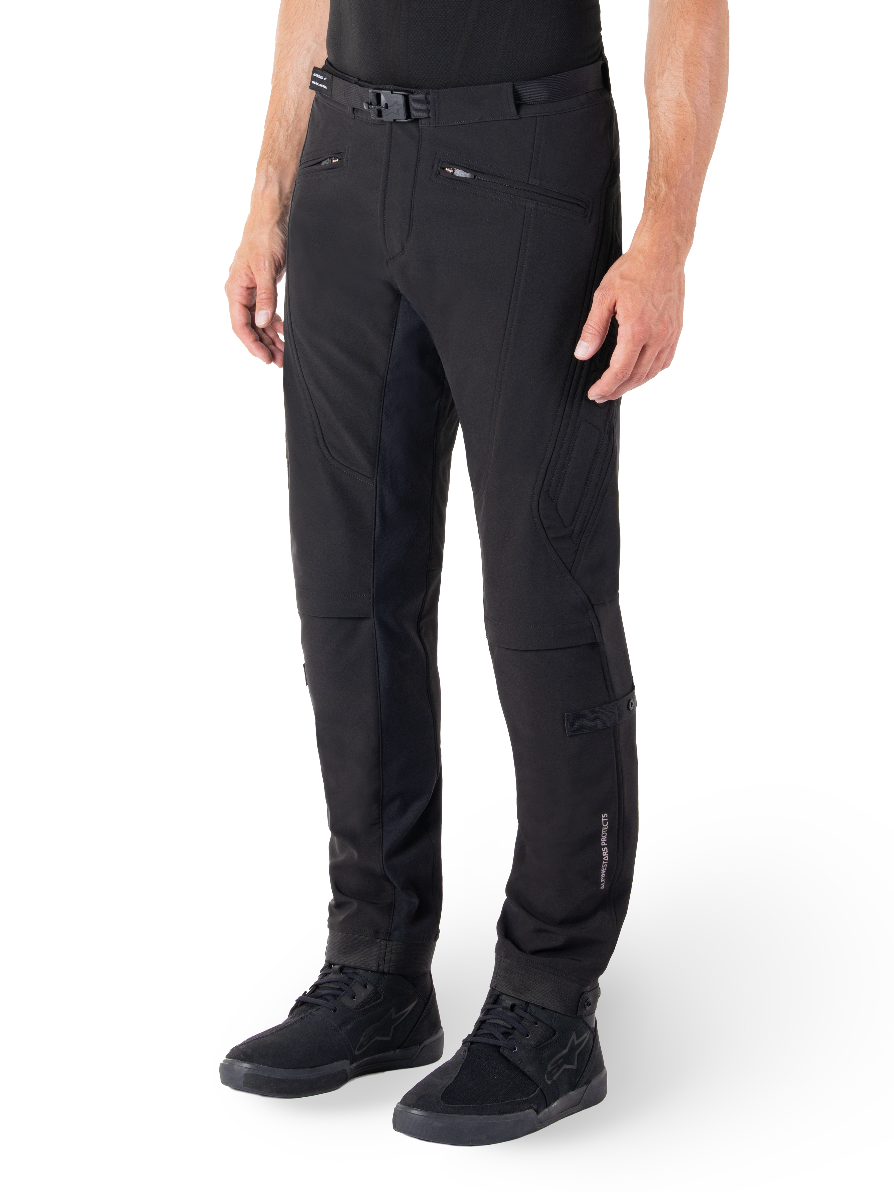 Alpinestars Alden Hose, Urbane Motorradhose, Schwarz, technisches Softshell-Gewebe mit normaler Passform, magnetische Gürtelschnalle, gesteppte Seiteneinsätze, Reißverschlusstaschen und dezentes Branding am Unterschenkel, getragen mit schwarzen Fahrerschuhen