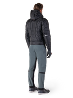 Alpinestars Alden Hose, urbane Motorradhose, Urban Gray, Rückansicht eines Fahrers in schwarzer gesteppter Kapuzenjacke und Motorrad-Sneakern, schmale Passform unterhalb des Knies mit schwarzen Stretcheinsätzen und Knieverstellern, modernes, von Streetwear inspiriertes Design.